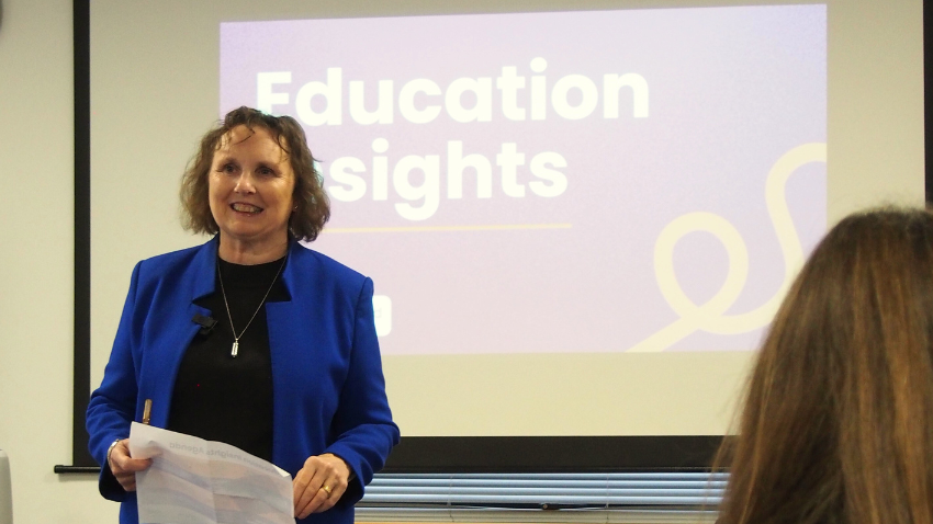 Speaker presenting at an Open Awards education insights session, standing in front of a screen while addressing an audience in a meeting room.