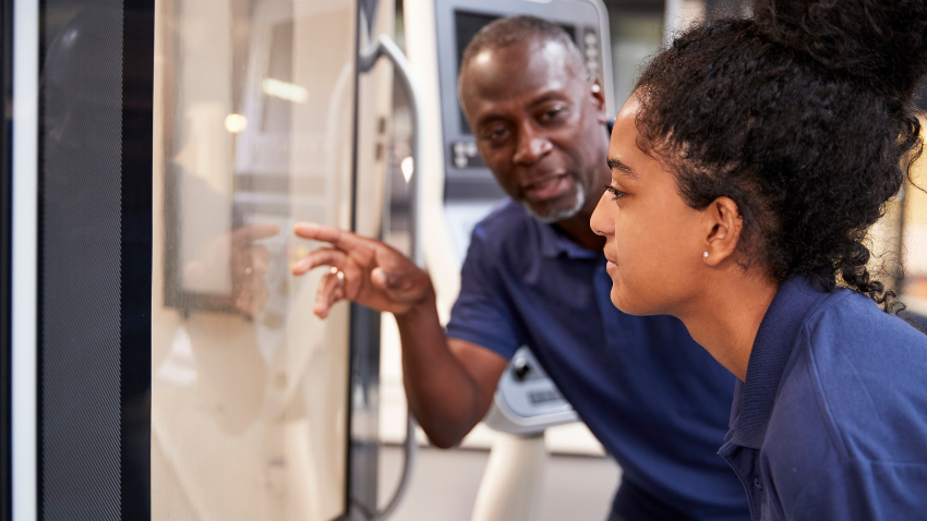 Tutor guiding a student through practical training on technical equipment, demonstrating hands on learning in a vocational education setting.